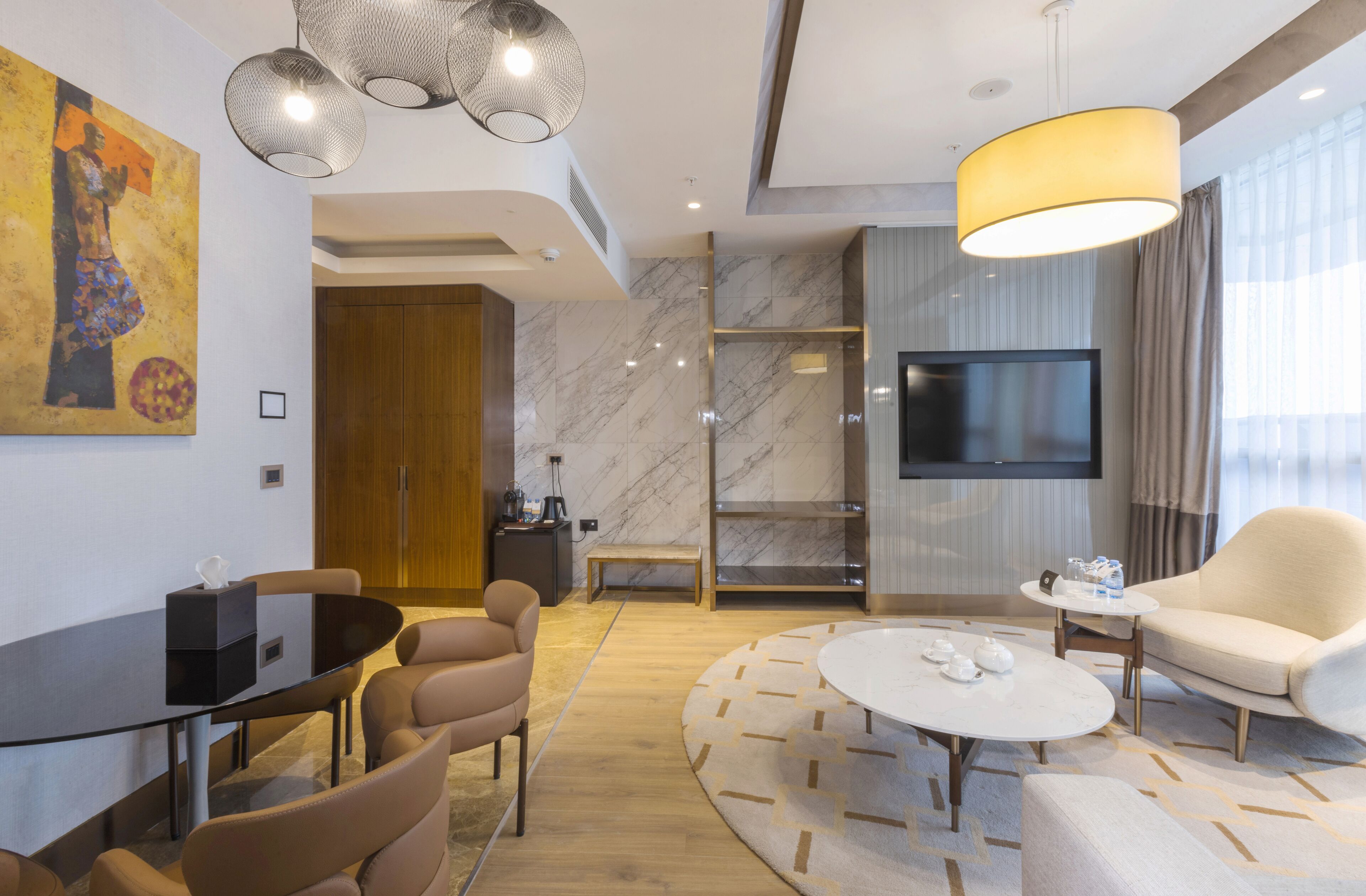 A modern hotel room with a marble floor, a round coffee table, a sofa, a TV, and a painting on the wall.