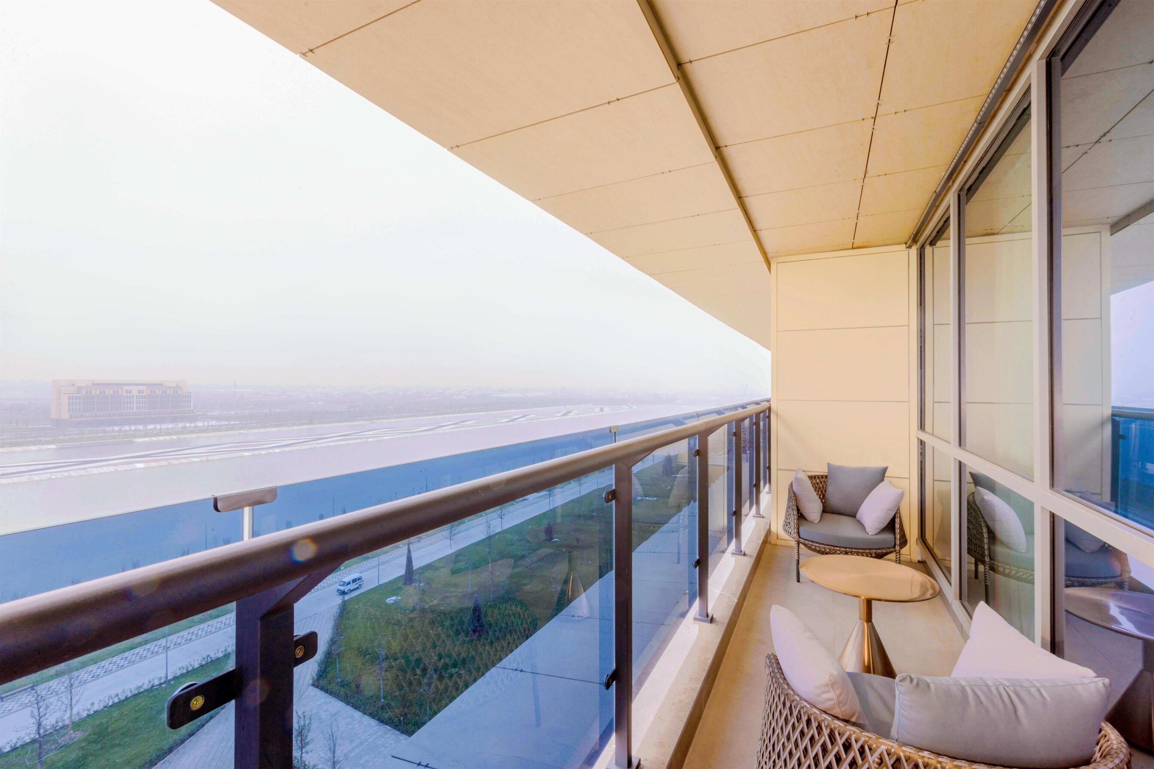 A balcony with a view of a bridge and river, wicker furniture, and a glass railing.