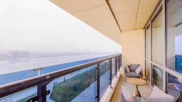 A balcony with a view of a bridge and river, wicker furniture, and a glass railing.