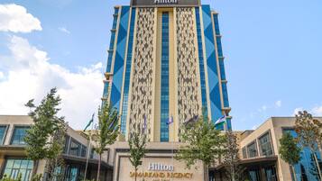 A tall, modern hotel building with a prominent Hilton logo and the name 'Samarkand Regency' displayed on the facade.