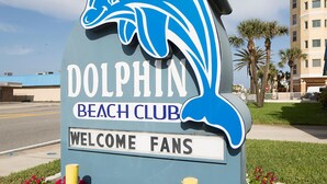 Letrero del Dolphin Beach Club, con logotipo de delfín y un mensaje de bienvenida para los aficionados.