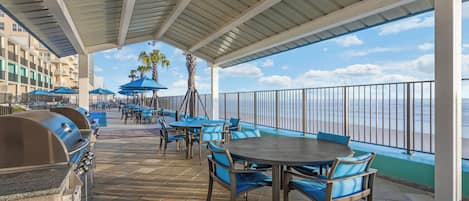 Un patio al aire libre con mesas y sillas, una parrilla y vista al océano.
