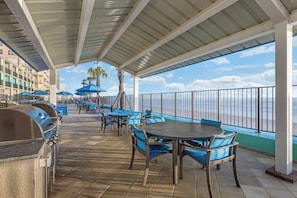 An outdoor patio with tables and chairs, a grill, and a view of the ocean. - Dolphin Beach Club (Daytona Beach)