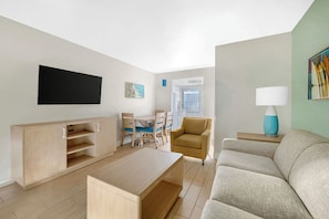 A modern living room with a flat-screen TV, a sofa, a coffee table, a dining area with chairs, and a lamp. - Dolphin Beach Club (Daytona Beach)