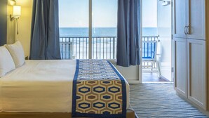 Una habitación de hotel con una cama grande, vista al océano, un balcón con una silla y un armario.