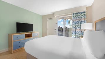Habitación de hotel con cama, televisor sobre una cómoda de madera, puerta que da a un balcón y cortina estampada.