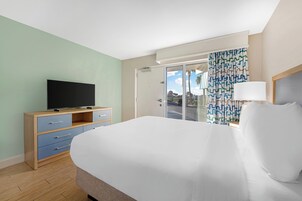 Et hotelværelse med en seng, et fjernsyn på en trækommode, en dør til en balkon og en stribet gardin.