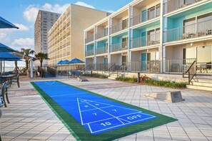 Un patio de hotel con una cancha de paletas, asientos al aire libre y un edificio de varios pisos con balcones.