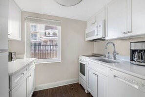 Una cocina moderna con armarios blancos, horno empotrado, microondas, cafetera y ventana con vista a un balcón.