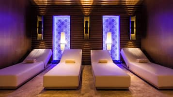 Relax in a serene spa room with two reclining massage chairs, a pillow, and a towel.
