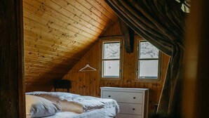 A bedroom with a wooden ceiling, a bed with white bedding, a dresser, and two windows.