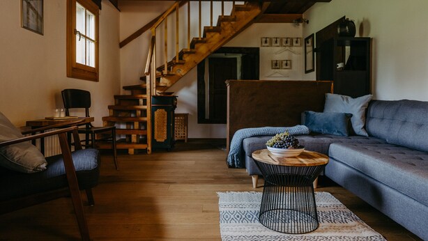 A cozy living room with a wooden staircase, a sofa, a coffee table, and a chair.