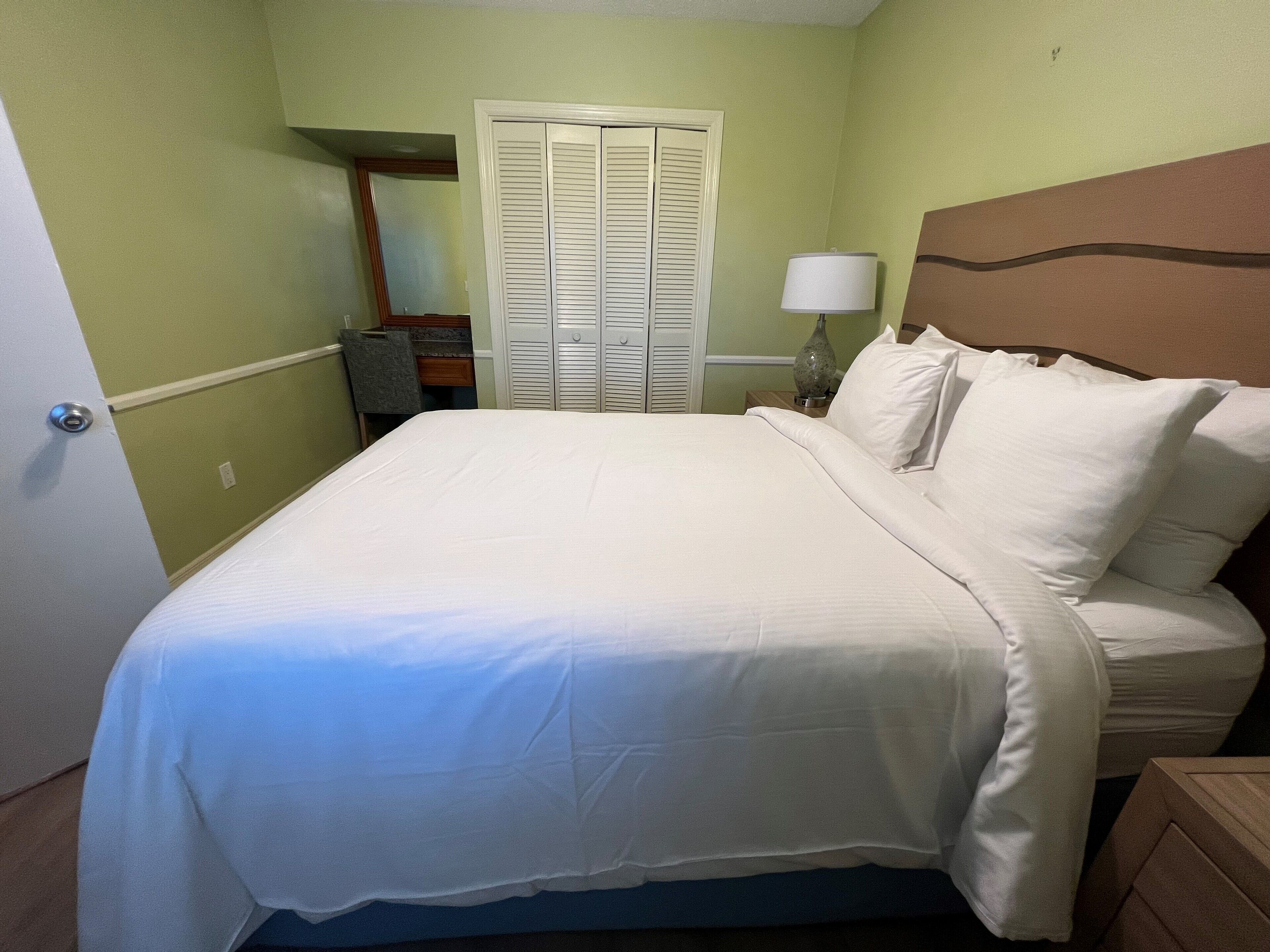 A neatly made bed with white linens in a room with green walls and a wooden headboard.