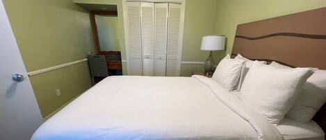 A neatly made bed with white linens in a room with green walls and a wooden headboard.