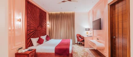 A hotel room with a large bed, a desk with a chair, a TV, and a wooden door.