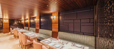 Un restaurant avec un plafond en bois, des banquettes confortables et une longue table à manger dressée avec des assiettes et des couverts.