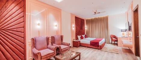 A modern hotel room with a large bed, two armchairs, a wooden coffee table, a desk with a chair, and a large mirror.