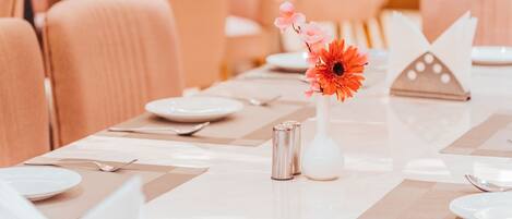 A dining table set with plates, cutlery, and a vase with flowers.