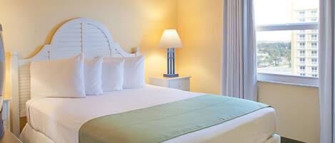 Una habitación de hotel con una cama, una mesita de noche con lámpara y una ventana con cortinas.