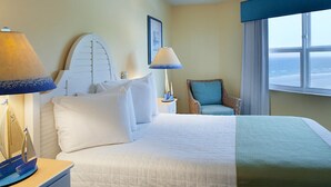 A hotel room with a bed, two bedside lamps, a chair, a nightstand, and a window with a view. - Fantasy Island II (Daytona Beach Shores)