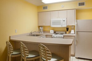 Cocina compacta con una isla central, microondas, estufa y refrigerador. Hay dos taburetes de bar y un lavamanos.