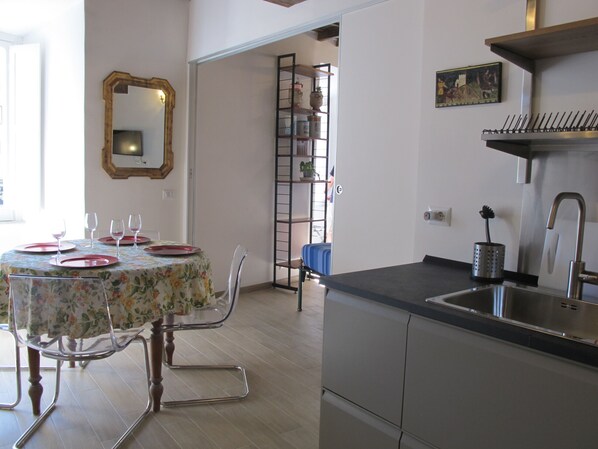 Un comedor con una mesa dispuesta para cuatro personas, un espejo y una cocina con un lavamanos y armarios.