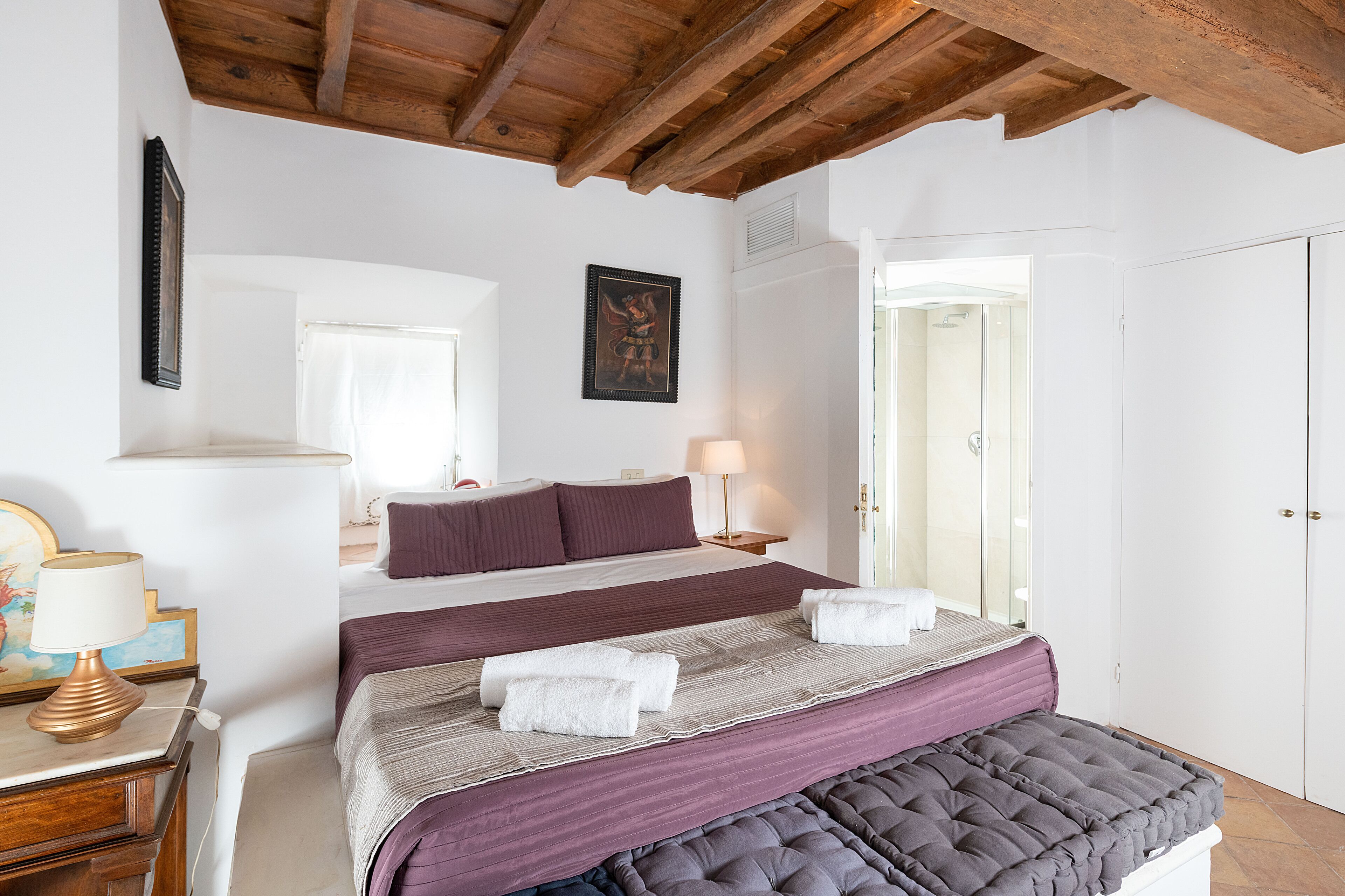 A bedroom with a large bed, a bedside table with a lamp, a wardrobe, and a painting on the wall.
