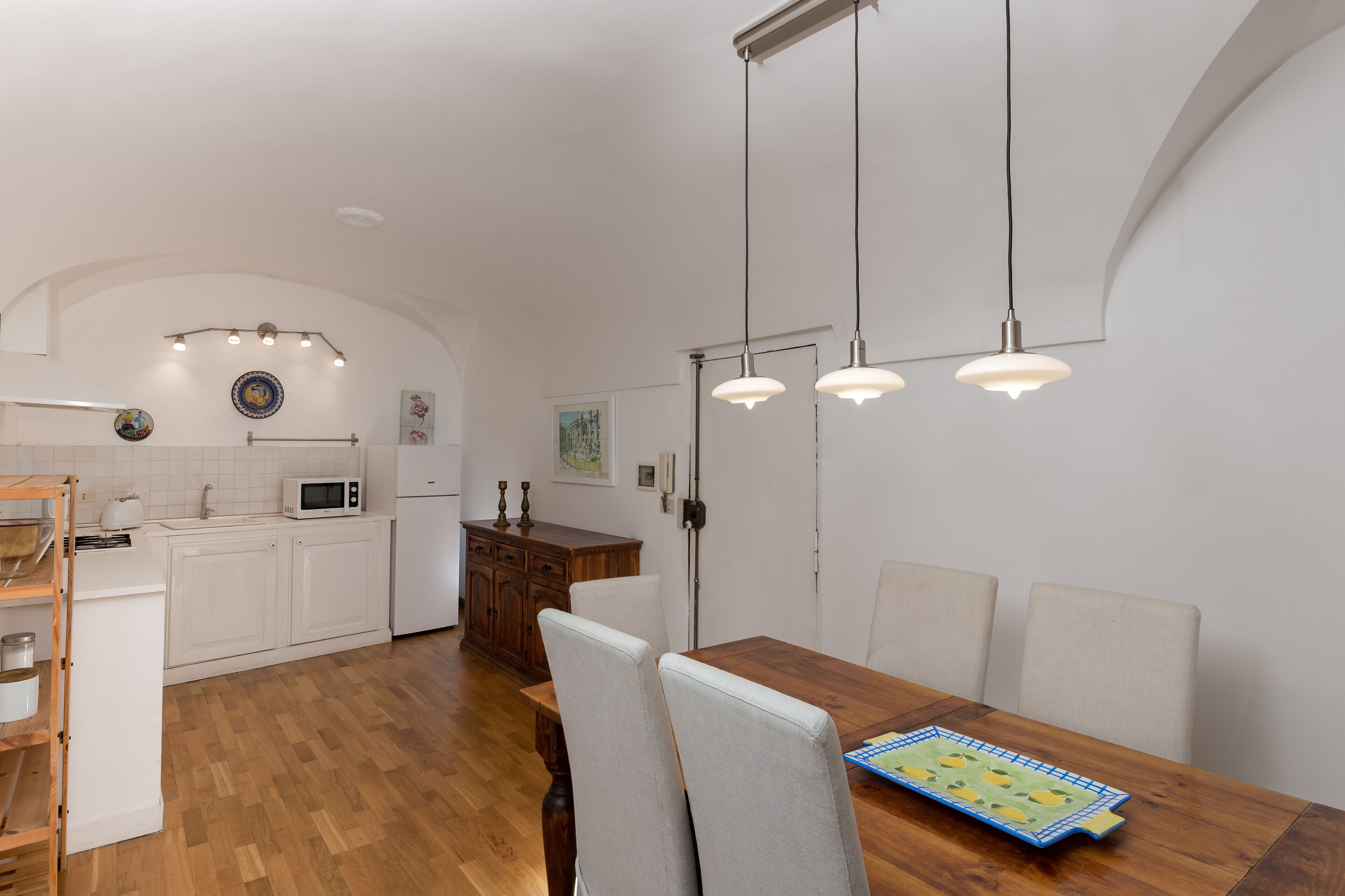 A modern kitchen with white cabinets, a wooden dining table, and pendant lighting.