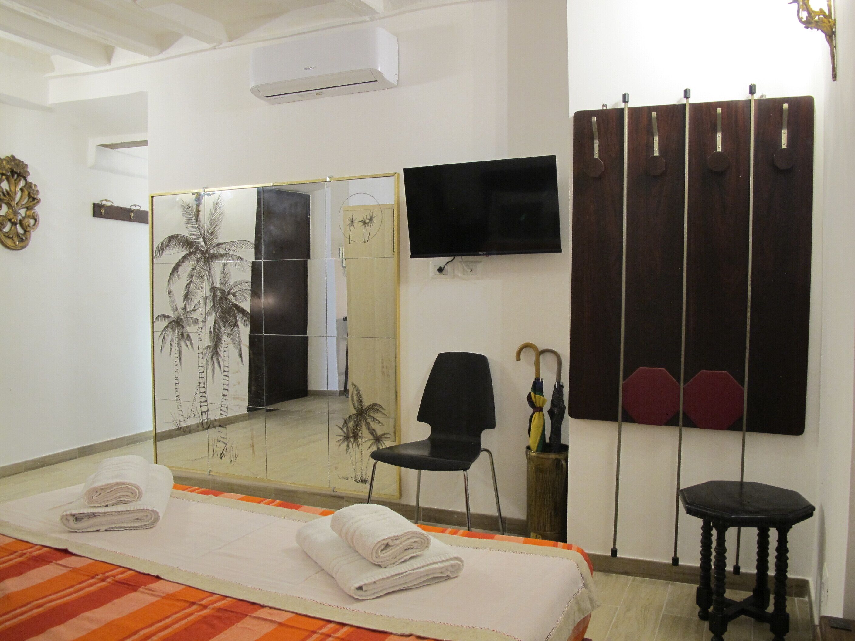 A hotel room with a bed, a chair, a TV, a mirror, and a wardrobe.