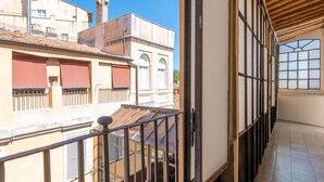 Un balcon donnant sur les bâtiments voisins, un plafond en bois et un sol carrelé.
