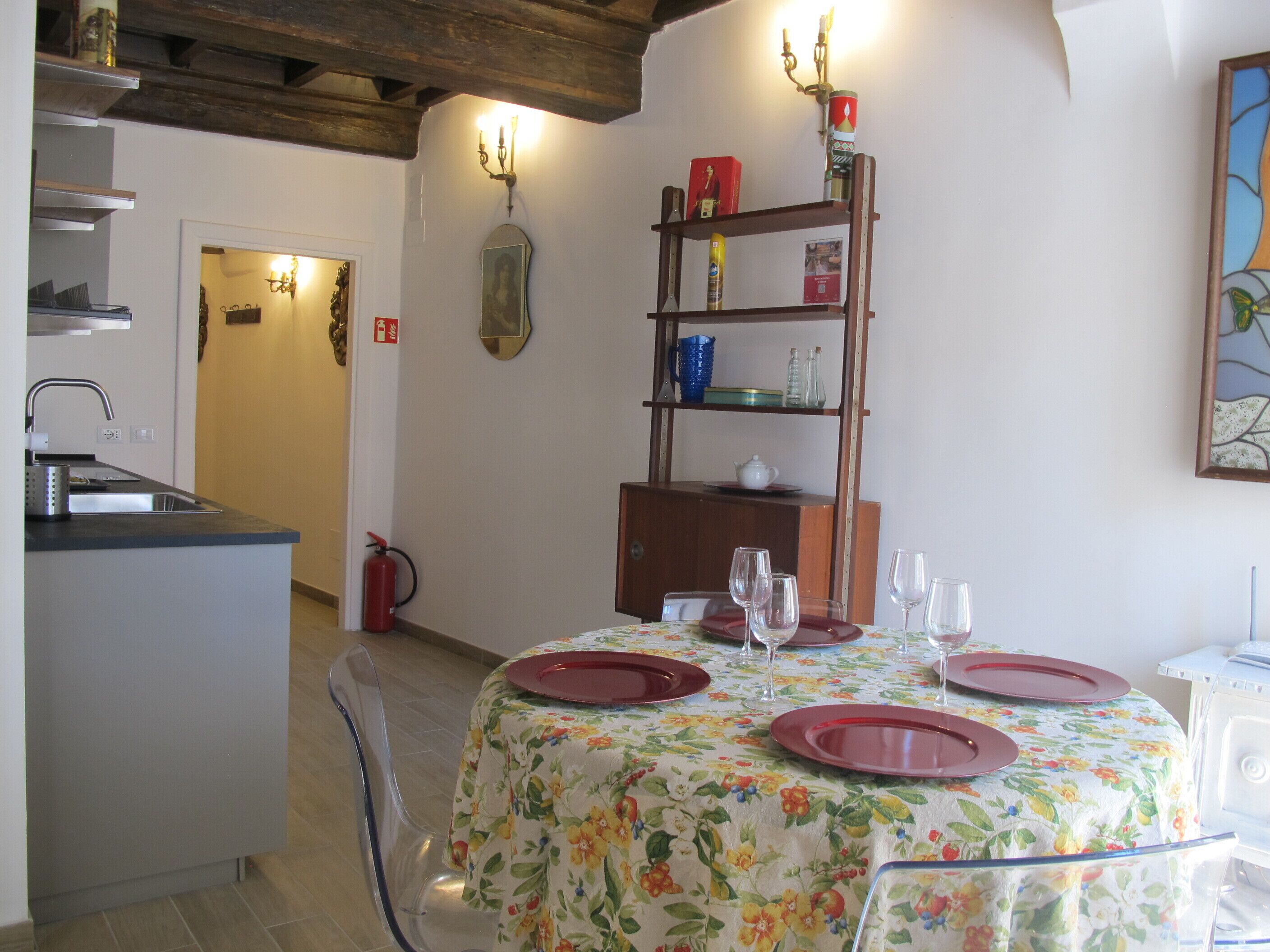 A dining area with a table set for four, a kitchen with a sink and a fire extinguisher, and a bookshelf with various items.