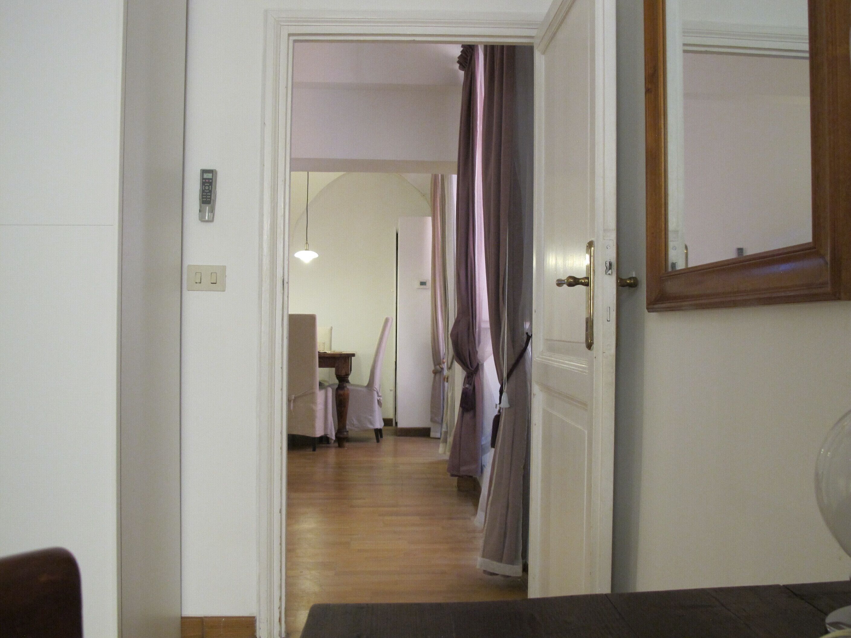 A hallway with a wooden floor, a dining area with a table and chairs, and a door with a mirror.