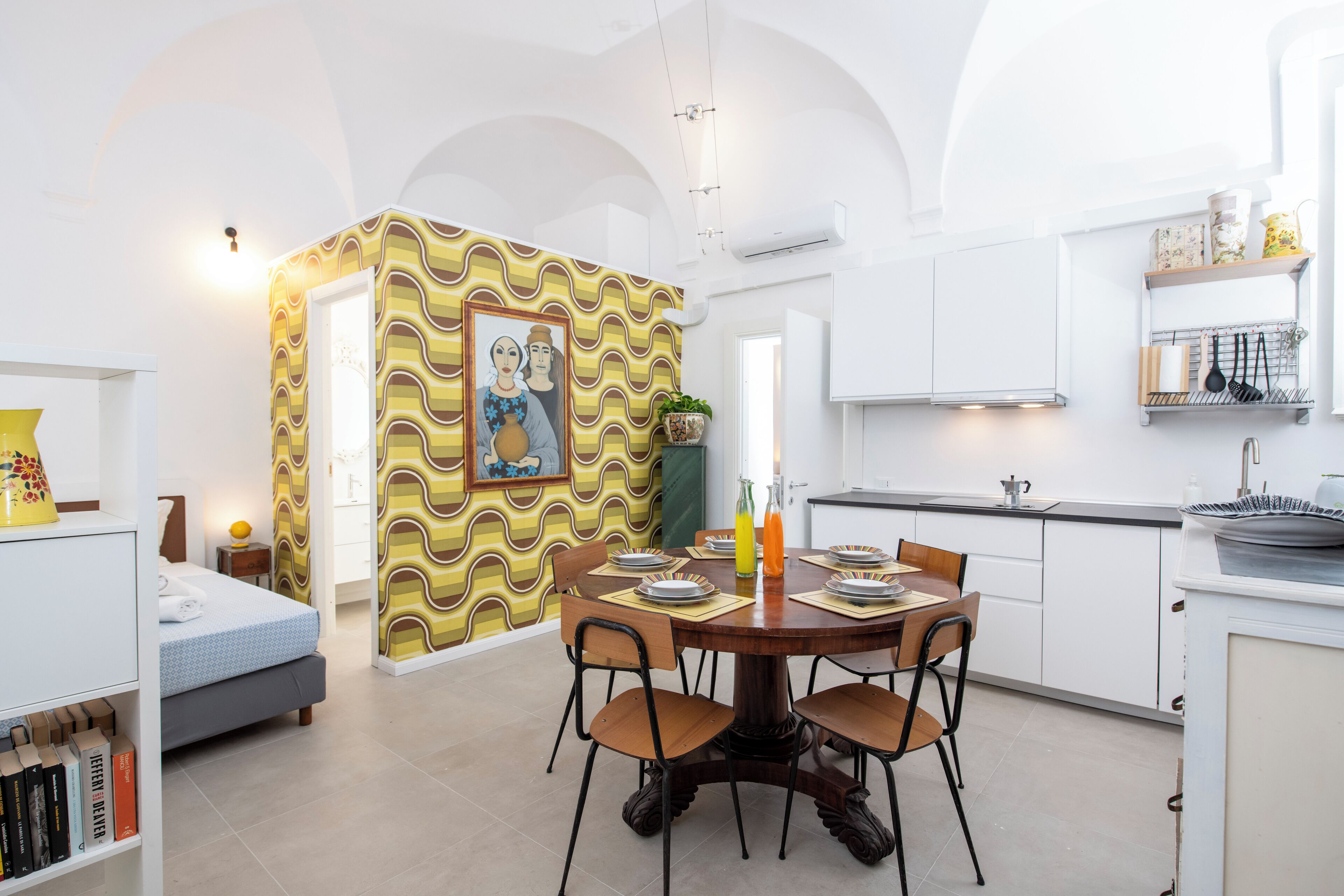 A modern kitchen with white cabinets, a dining table with chairs, and a patterned wall.