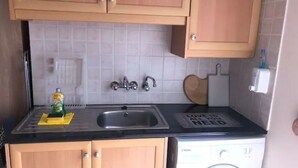 A compact kitchen with wooden cabinets, a sink, a washing machine, and a countertop with a bottle of dish soap.