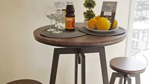 A dining area with a round table, two stools, a bottle of Zima, a small potted plant, and a framed picture.