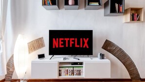 Un salón con un televisor de pantalla plana mostrando el logotipo de Netflix, un mueble blanco para entretenimiento con estanterías y una pared de acento de madera.