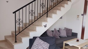 A staircase with a black railing and decorative elements, a grey sofa with multiple cushions, and a small wooden table with a white cloth.