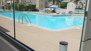 A swimming pool with a clear blue water, surrounded by lounge chairs and umbrellas, and a tiled deck area.