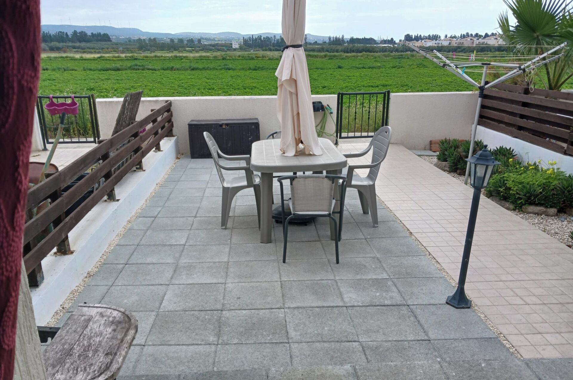 Un patio exterior con mesa y sillas, una valla de madera y vistas a un campo verde.