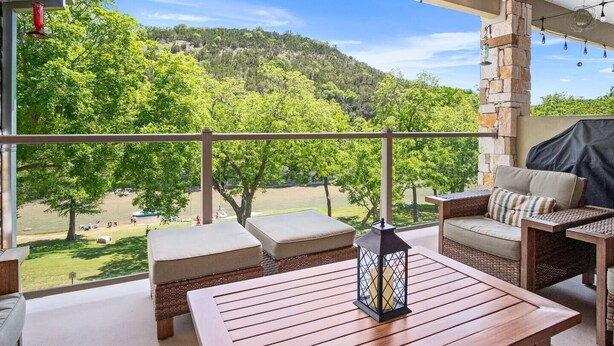 A balcony with wicker furniture, a wooden table, and a lantern. - 2/2 Condo Directly on the Guadalupe River with Beautiful Canyon Views (New Braunfels)