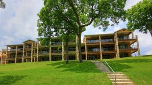 A multi-story hotel with a central courtyard, a staircase leading to the entrance, and a lush green lawn. - 2/2 Condo Directly on the Guadalupe River with Beautiful Canyon Views (New Braunfels)