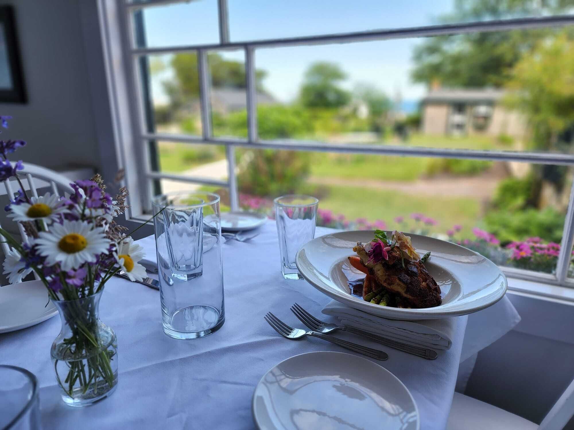 Ein Tisch ist für eine Mahlzeit gedeckt, mit einer Speisenplatte, einem Blumenstrauß und klaren Gläsern.