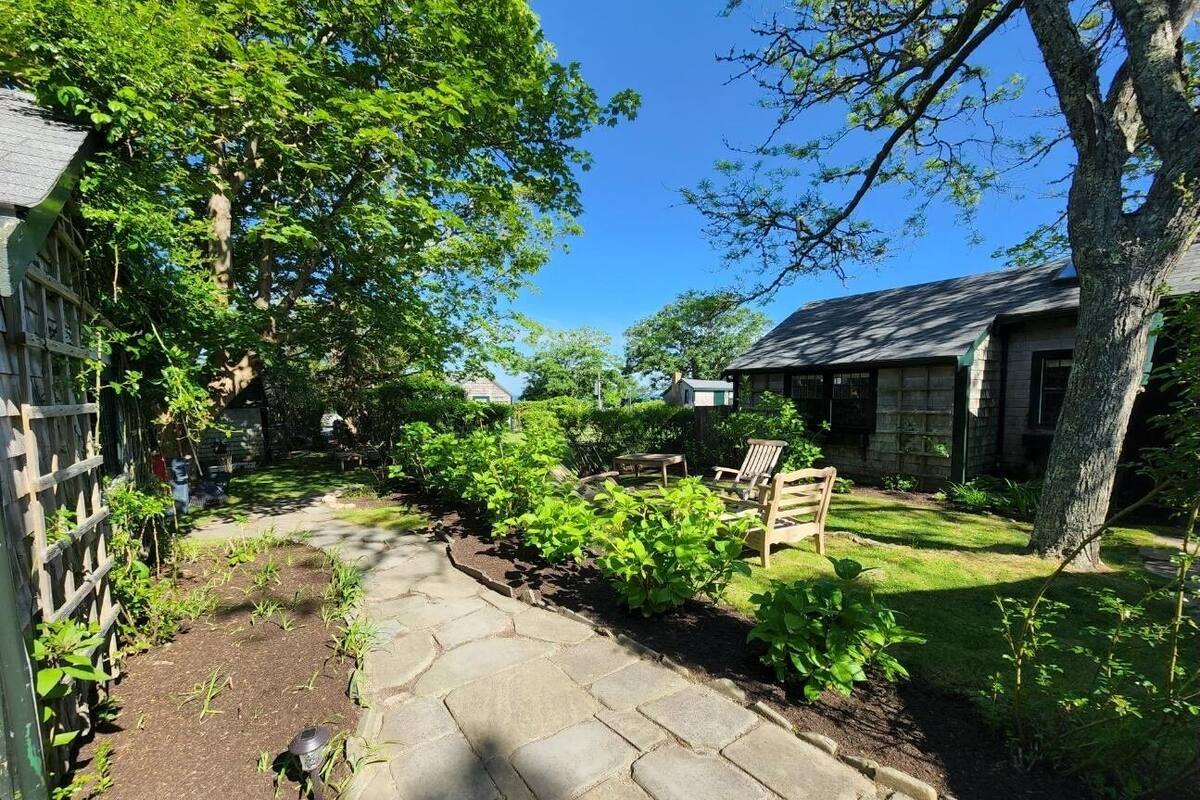 A stone pathway leading through a garden with a wooden bench and a small table.