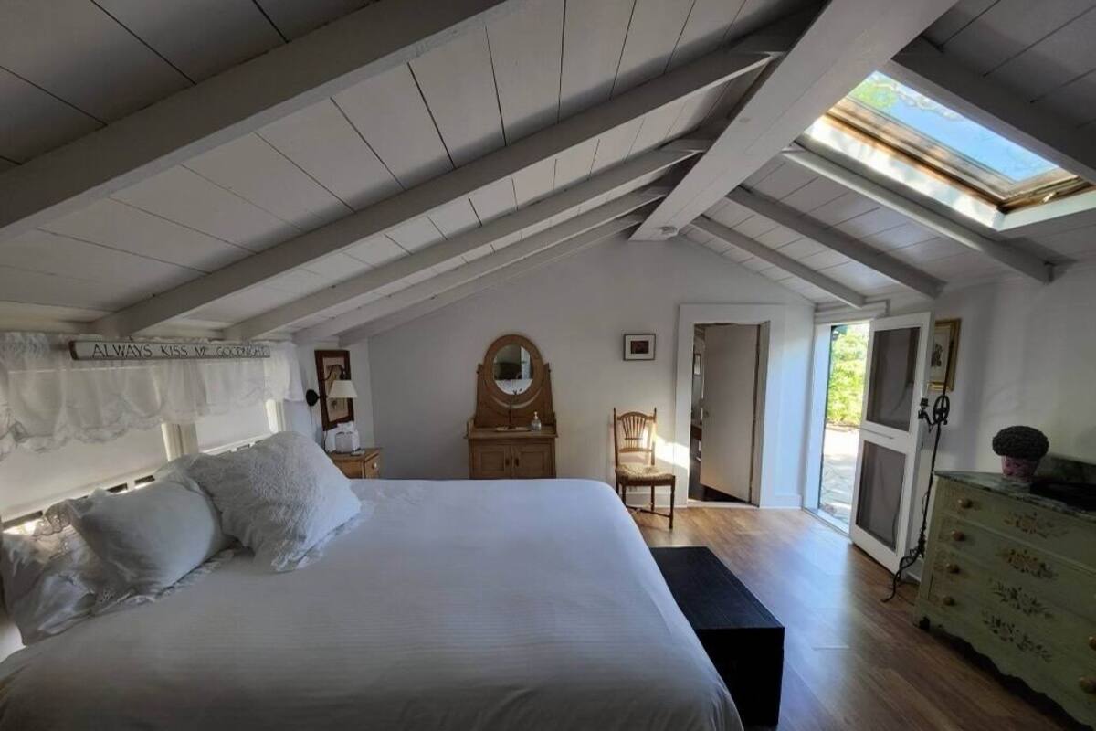 A bedroom with a large bed, a wooden dresser, a chair, and a skylight.