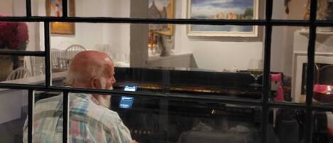 A person playing a piano inside a room with a glass partition.