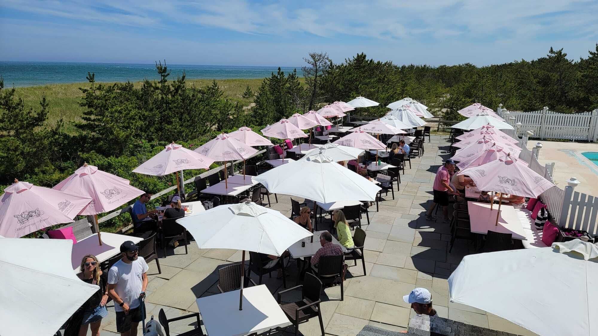 Un espace de restauration en plein air, avec des tables et des parasols, offrant une vue sur un plan d’eau et une végétation luxuriante.