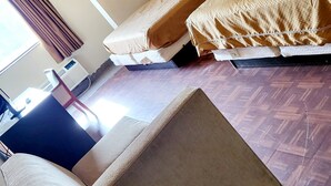 Ein Hotelzimmer mit zwei Betten, einem Holzkopfende, einem Fenster mit Vorhängen und Holzboden.