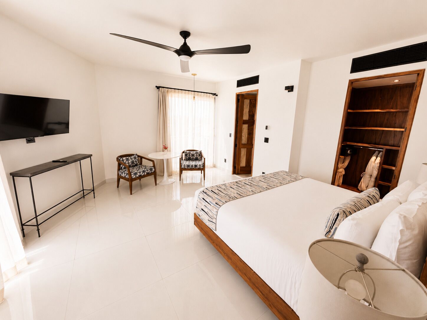 Habitación de hotel con cama, escritorio, silla, televisor, ventilador de techo y armario.