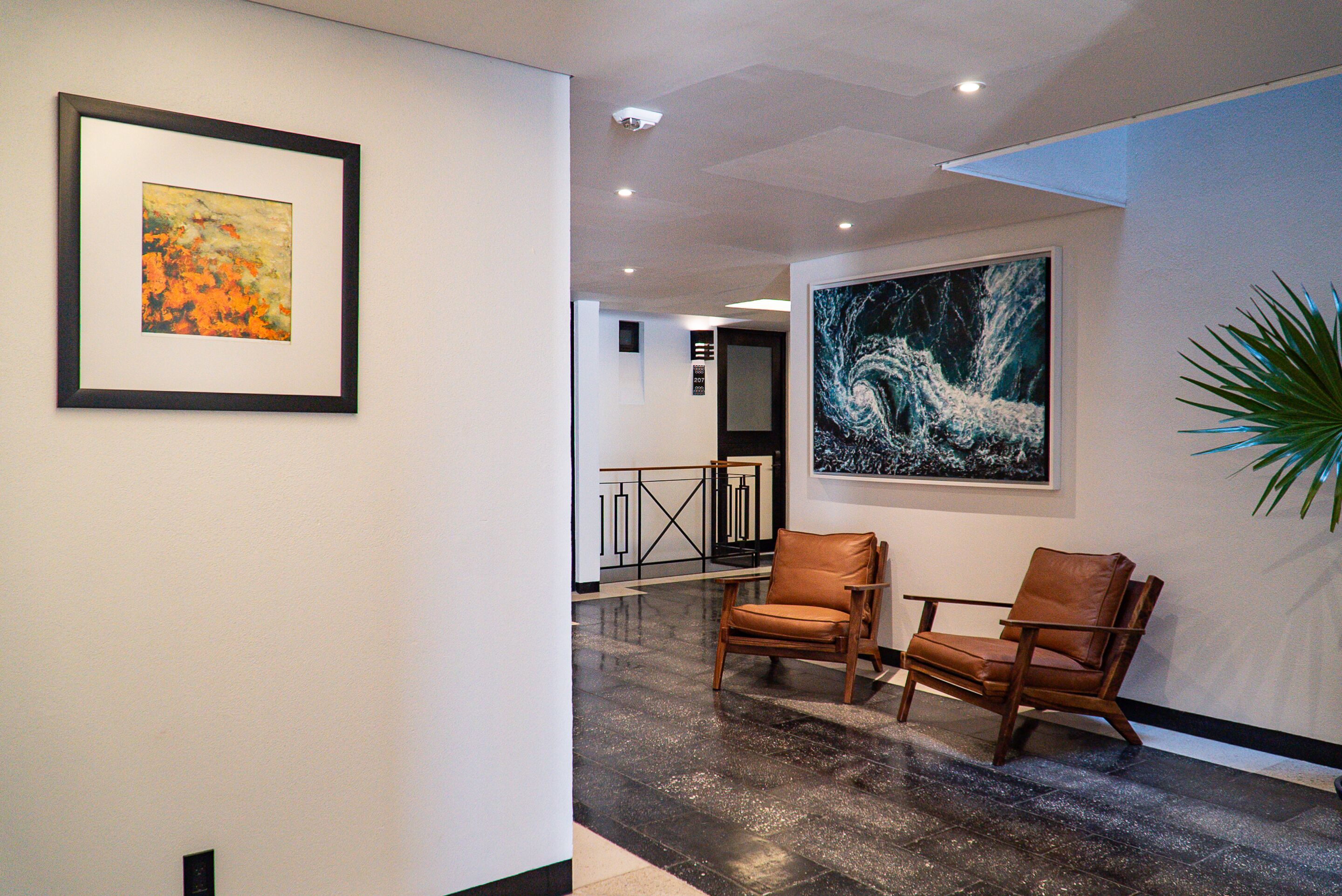 A hallway with two leather chairs, a framed abstract painting, and a large wave-themed artwork on the wall.