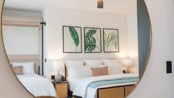 Habitación de hotel con cama, dos mesitas de noche, un espejo y tres cuadros con hojas enmarcadas en la pared.